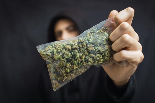 Hooded man holding a big bag of weed on black background.