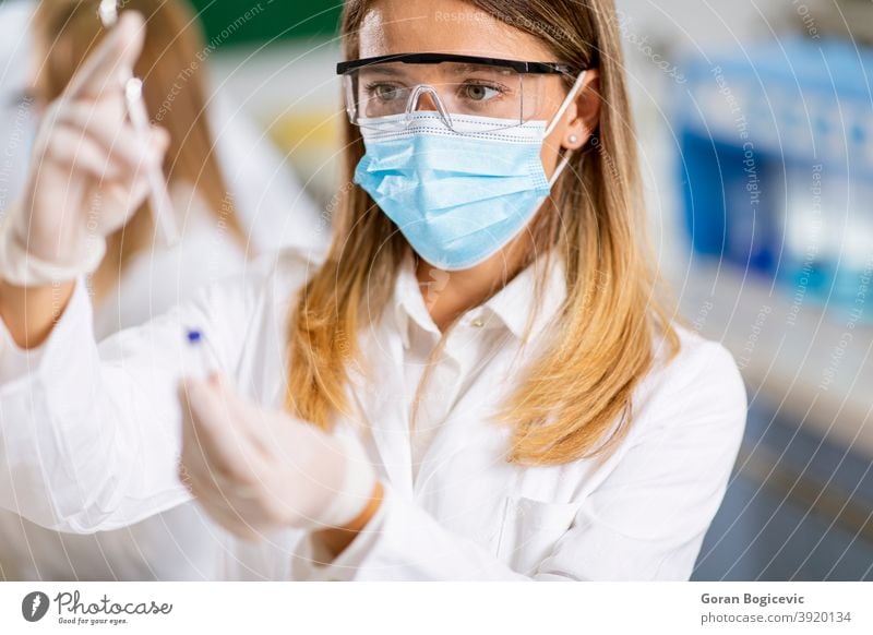 Woman doctor wearing protective face mask in lab hold needle syringe ...