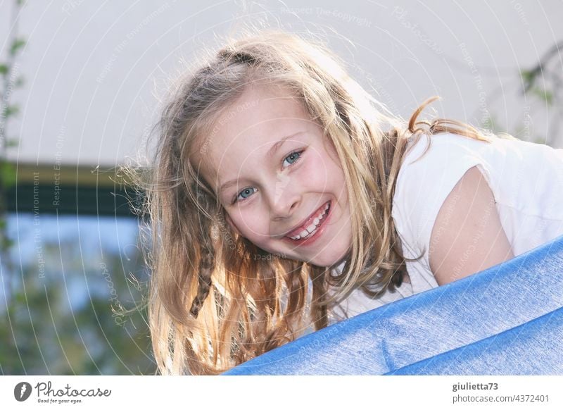 Portrait of a happy, laughing 8 year old girl with long blond hair playing  on the slide - a Royalty Free Stock Photo from Photocase